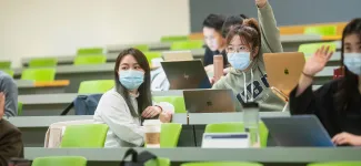 A student sitting in class raises a hand.